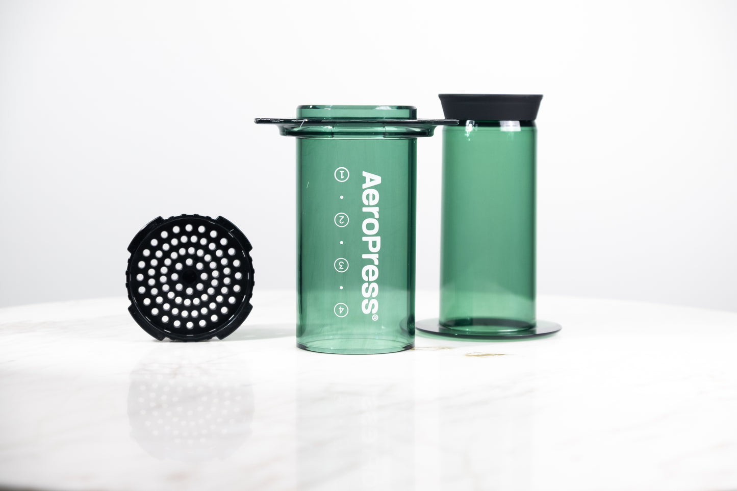 Cafetera manual AeroPress Clear en color verde translúcido. Despiece del método de preparación que incluye cámara, émbolo y tapa de filtro para café de especialidad.