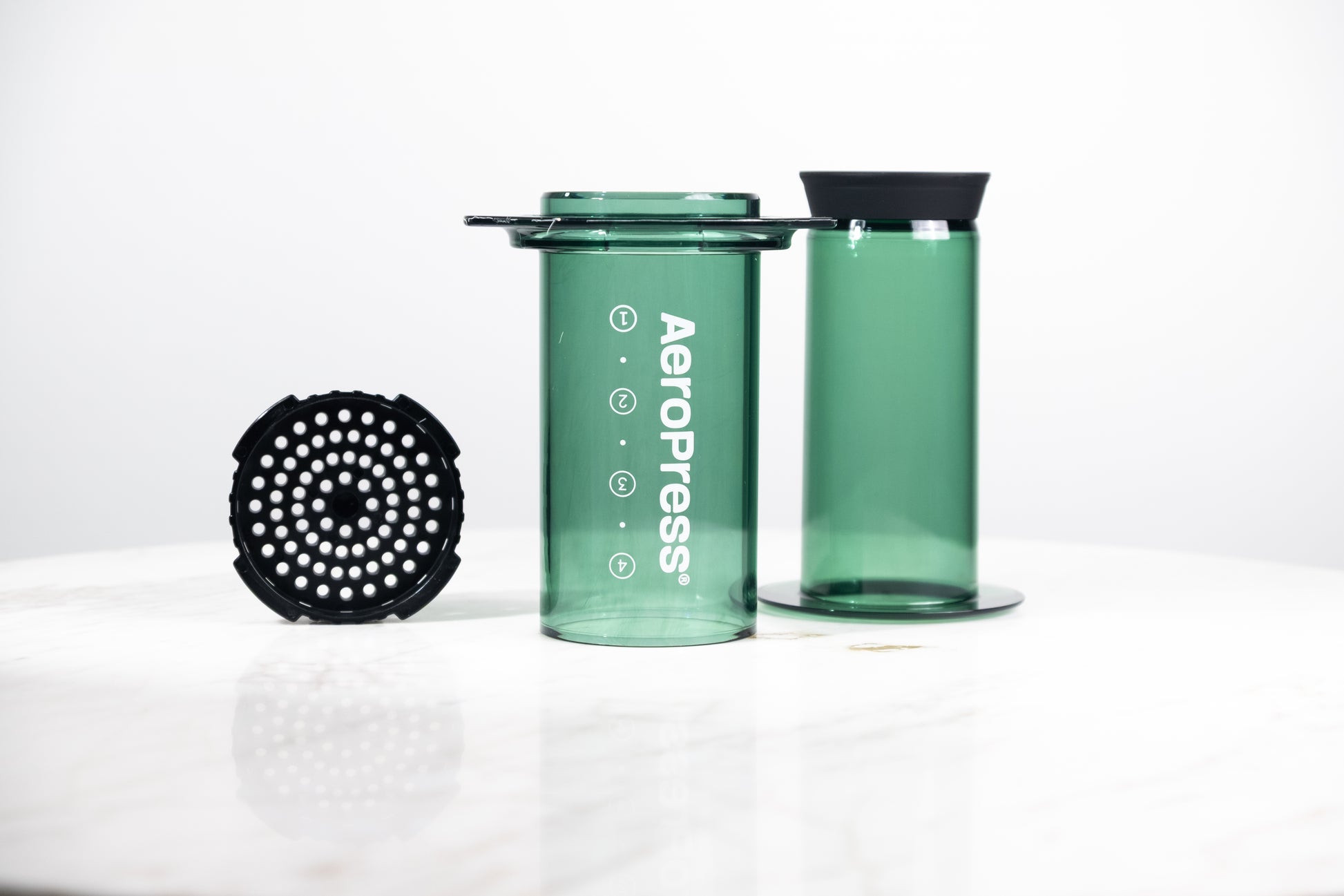 Cafetera manual AeroPress Clear en color verde translúcido. Despiece del método de preparación que incluye cámara, émbolo y tapa de filtro para café de especialidad.