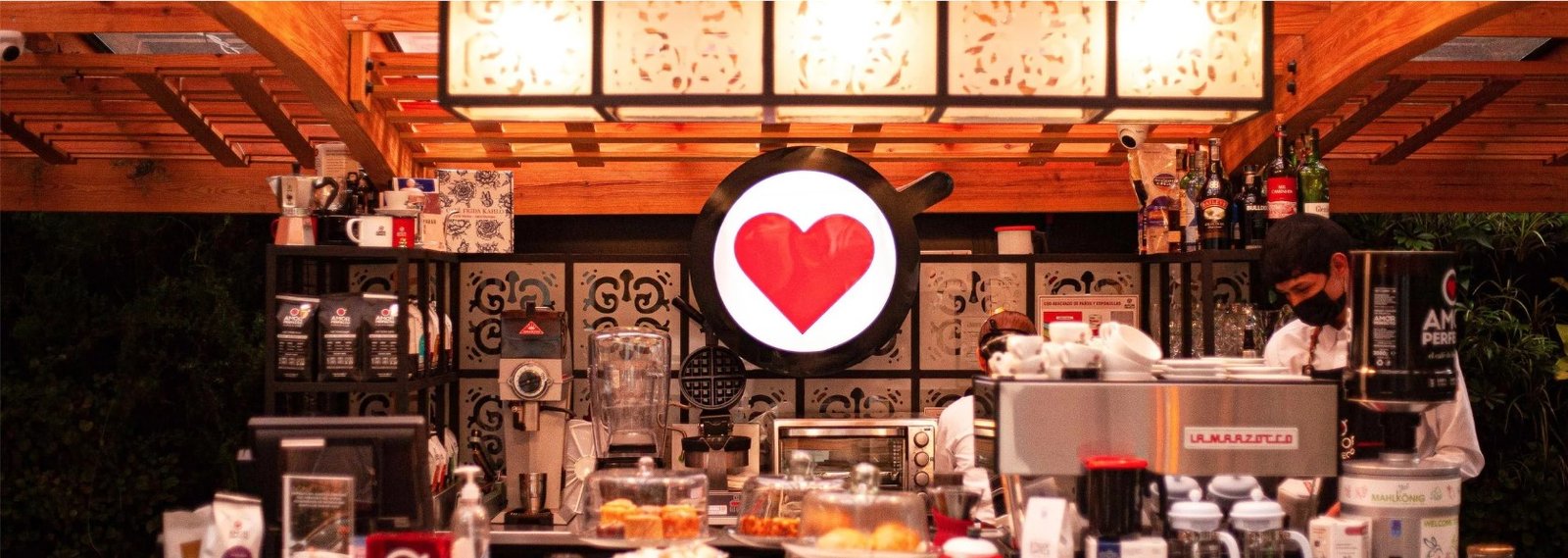 Barista preparando café de especialidad Amor Perfecto en barra profesional con máquina La Marzocco y exhibición de café premium.