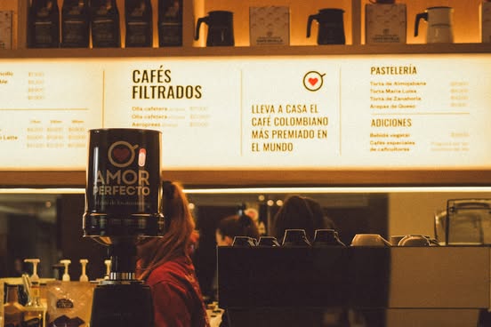 Barra de café de especialidad Amor Perfecto con menú de cafés filtrados y pastelería. Fotografía de tienda física destacando el café colombiano más premiado en el mundo.