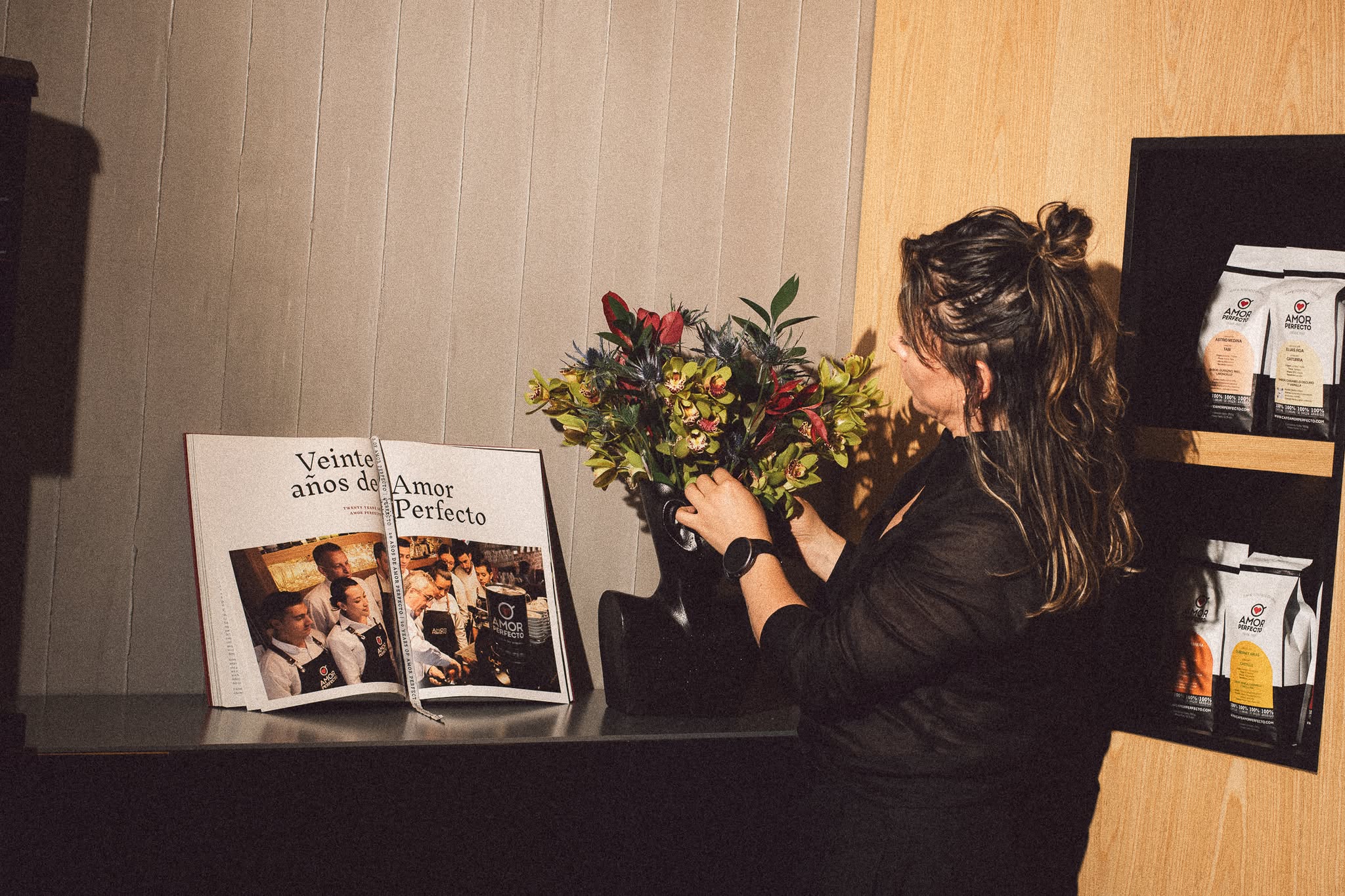 Libro "Veinte años de Amor Perfecto" en un ambiente elegante con flores y bolsas de café de especialidad. Fotografía que celebra la historia y cultura del café colombiano de alta calidad.